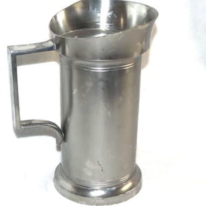 May include: A silver pewter pitcher with a handle. The pitcher has a rounded top and a cylindrical body.