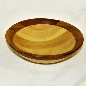 May include: A wooden bowl with a light brown interior and a dark brown rim. The bowl is made of different types of wood, creating a unique pattern.