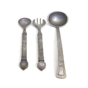 May include: A set of three silver-toned kitchen utensils: a spoon, a fork, and a ladle. Each utensil has a hammered texture and a decorative knob at the end of the handle.