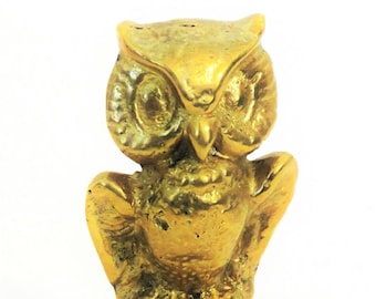 May include: A small, golden-colored owl figurine with detailed features. The owl has large eyes, a beak, and outstretched wings. The figurine is made of a metallic material and stands on a textured base. The owl is a decorative item.