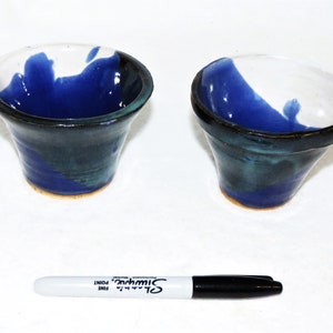 May include: Two small ceramic bowls with a blue and green glaze. The bowls are slightly flared at the top and have a rounded bottom.