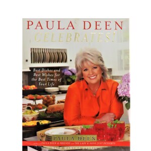 May include: A cookbook cover featuring Paula Deen, a well-known chef, smiling and leaning on a table with a variety of dishes. The title of the book is "Paula Deen Celebrates! Best Dishes and Best Wishes for the Best Times of Your Life."
