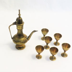 May include: A set of six small gold-colored metal cups and a matching pitcher with a lid. The pitcher has a spout and a handle.