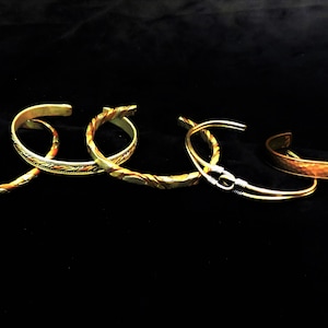 May include: Five different metal bracelets, some with intricate designs, in shades of gold and copper.