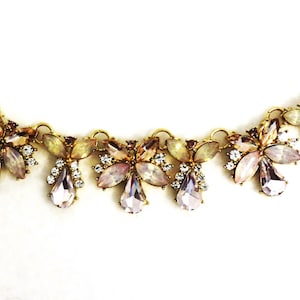 May include: A gold chain necklace with a delicate design featuring multiple teardrop-shaped crystals in shades of pink and white.