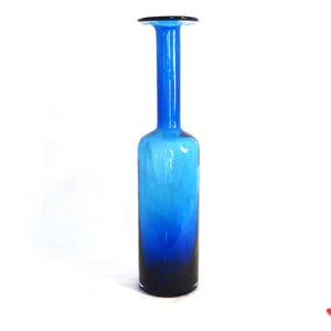 May include: A tall, slender blue glass vase with a flared top. The vase has a gradient of color, starting with a lighter blue at the top and transitioning to a darker blue at the bottom.