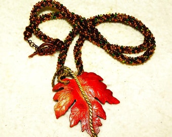 May include: A necklace with a copper leaf pendant. The necklace is made of brown and green beads. The leaf is a vibrant orange color.