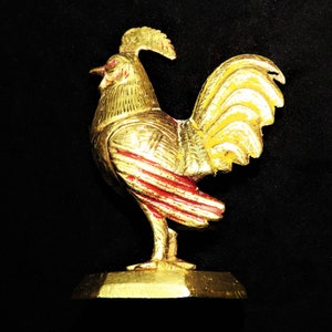 May include: A gold rooster figurine with red and gold accents standing on a gold base. The rooster is facing the right side of the image.