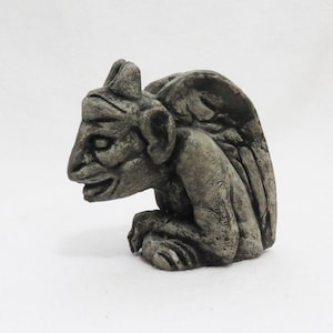 May include: A gray stone gargoyle sculpture with a wing, a pointed ear, and a snarling expression.