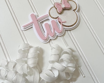 Può includere: Topper per torta con glitter rosa e oro con la parola "due" e una testa di Minnie Mouse rosa e bianca con un fiocco.