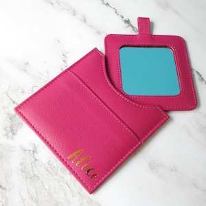 May include: A pink compact mirror with a gold inscription that reads "Alice". The mirror is closed and the inscription is visible on the front.