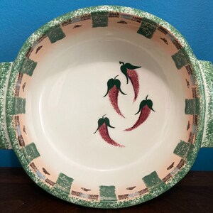 May include: A white ceramic baking dish with green and brown trim. The dish has a scalloped edge and features a design of red chili peppers.