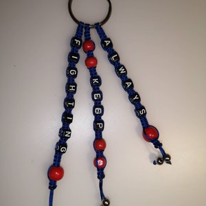 Może przedstawiać: Brelok do kluczy z niebieskimi i czerwonymi koralikami z napisem "Always Keep Fighting".