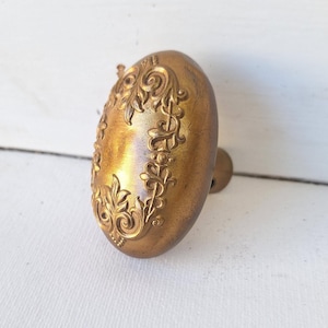 May include: A gold-toned oval door knob with an ornate floral design.