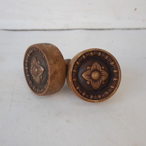 May include: Two antique brass door knobs with a decorative floral design. The knobs are round and have a raised edge.