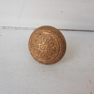May include: A gold-toned metal knob with an intricate floral design.
