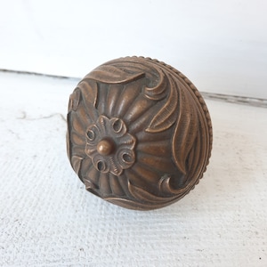 May include: A round, ornate, bronze door knob with a floral design.