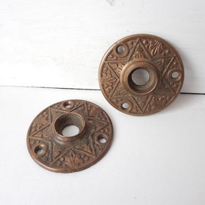 May include: Two antique brass door knobs with intricate star and floral designs. The knobs are round and have a hole in the center for a door handle.