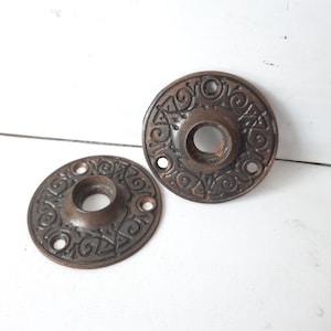 May include: Two antique door knobs with intricate designs. The knobs are made of metal and have a dark brown finish.