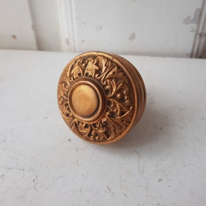 May include: A vintage, ornate, gold-toned door knob with a detailed floral design.