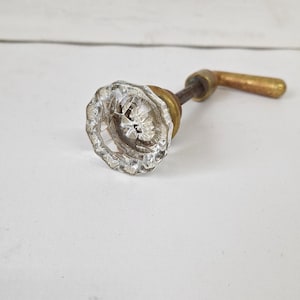 May include: A vintage glass door knob with a brass handle. The knob is clear glass with a faceted design.
