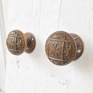 May include: A pair of antique brass door knobs with intricate floral designs. The knobs are round and have a textured surface.