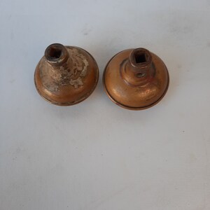 May include: Two antique brass door knobs with square inserts. The knobs are slightly tarnished and have a worn finish.