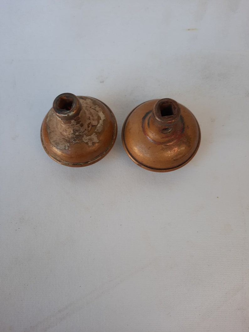 May include: Two antique brass door knobs with square inserts. The knobs are slightly tarnished and have a worn finish.