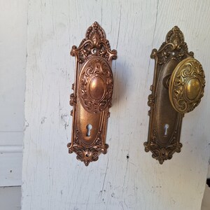 Puede incluir: Dos juegos de manijas de puerta antiguas. Uno es de color cobre con un centro ovalado y detalles ornamentados. El otro es de color lat&oacute;n con un mango redondo y elementos decorativos similares. Ambos tienen cerraduras.