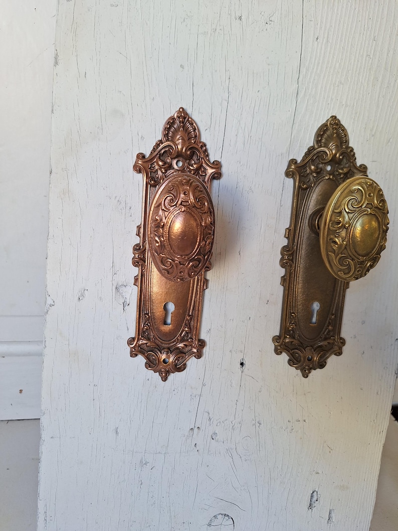 Puede incluir: Dos juegos de manijas de puerta antiguas. Uno es de color cobre con un centro ovalado y detalles ornamentados. El otro es de color lat&oacute;n con un mango redondo y elementos decorativos similares. Ambos tienen cerraduras.