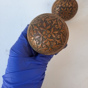 May include: Two antique brass door knobs with intricate floral designs.