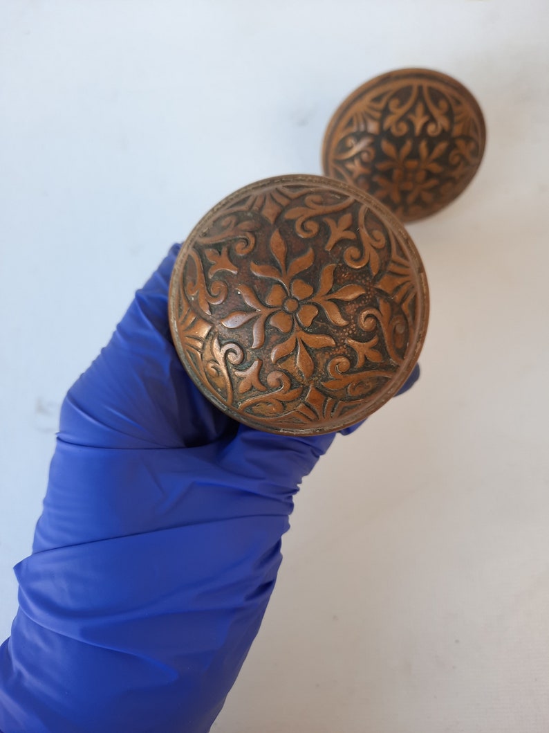 May include: Two antique brass door knobs with intricate floral designs.