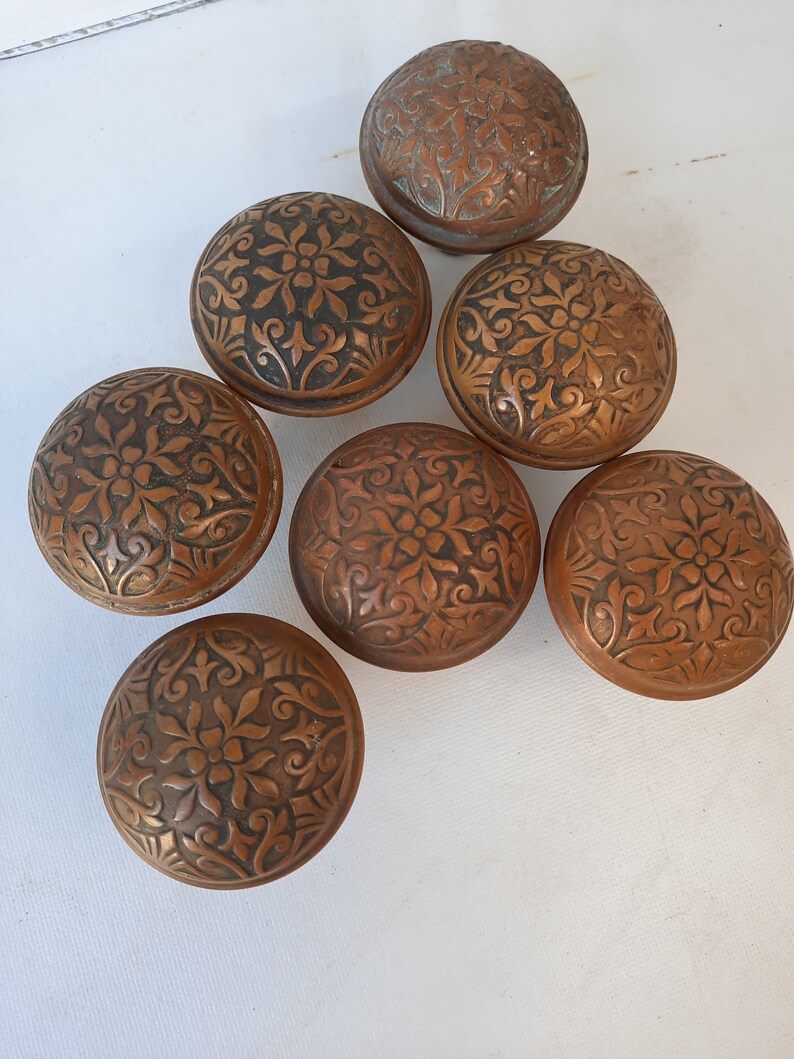 May include: Six antique door knobs with intricate floral designs. The knobs are made of a dark copper metal and have a worn, aged finish.
