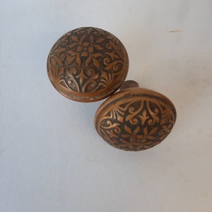 May include: Two antique door knobs with intricate floral designs. The knobs are made of a dark brown metal and have a worn, aged appearance.