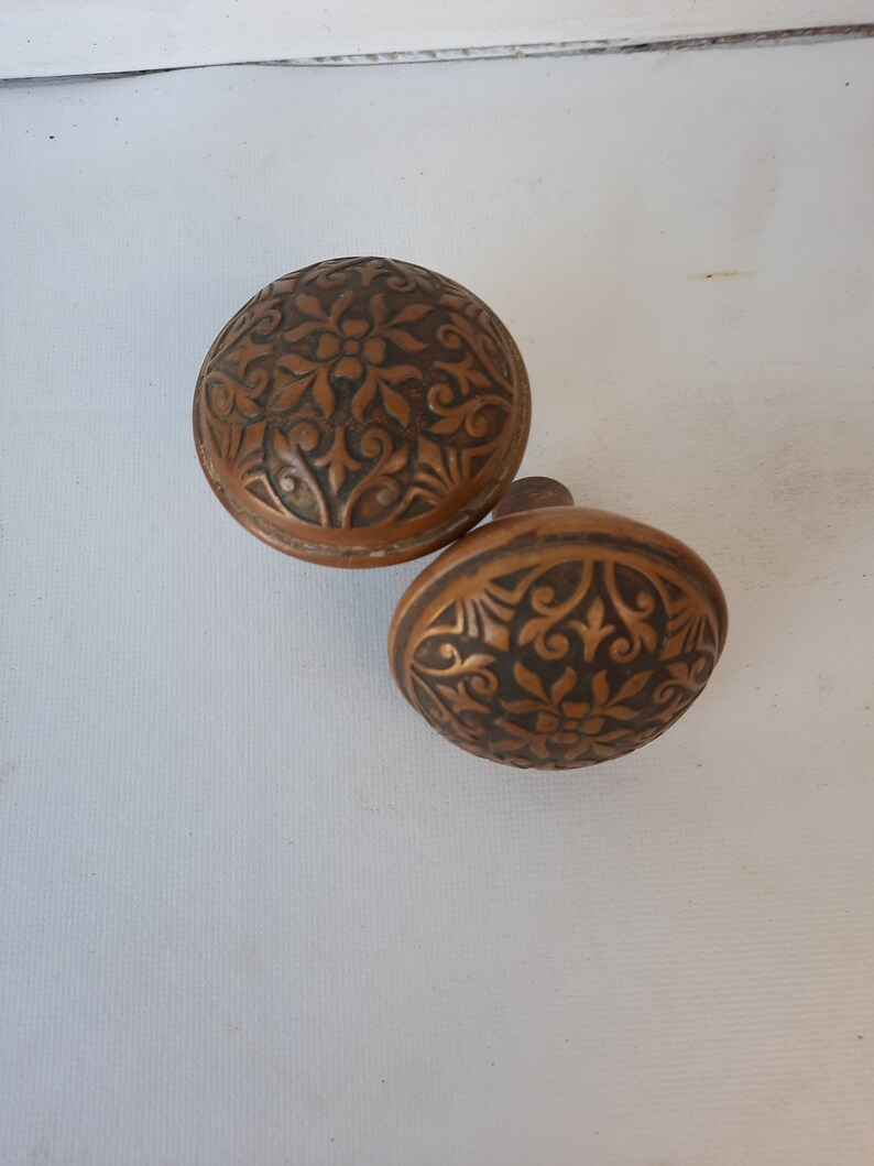 May include: Two antique door knobs with intricate floral designs. The knobs are made of a dark brown metal and have a worn, aged appearance.
