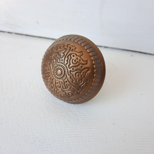 May include: A round, copper-colored door knob with an intricate, embossed floral design.