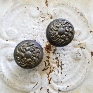 May include: Two antique-style door knobs with ornate floral designs on a white, cracked, and rusty surface.
