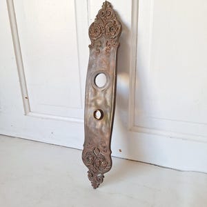 May include: Ornate antique brass door plate with two keyholes and intricate floral designs.