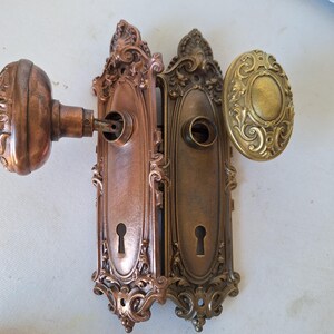 Puede incluir: Juego de herrajes de puerta antiguos con dos placas de puerta de bronce ornamentadas con cerraduras y un pomo de puerta de bronce a juego. El juego incluye un pomo de puerta ovalado de lat&oacute;n. El herraje tiene un aspecto envejecido y vintage.