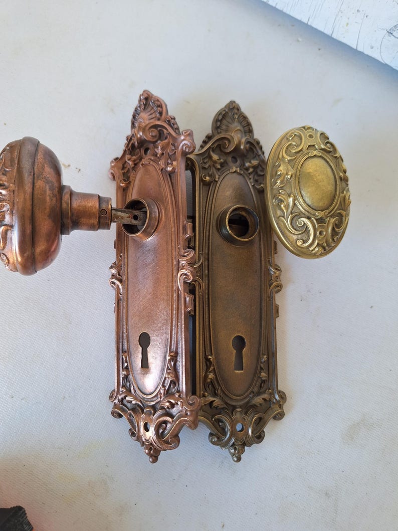 Puede incluir: Juego de herrajes de puerta antiguos con dos placas de puerta de bronce ornamentadas con cerraduras y un pomo de puerta de bronce a juego. El juego incluye un pomo de puerta ovalado de lat&oacute;n. El herraje tiene un aspecto envejecido y vintage.