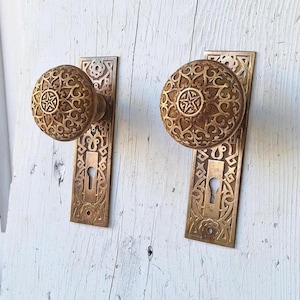 May include: A pair of antique brass door knobs with intricate floral designs and keyholes. The knobs are mounted on rectangular plates with matching designs.