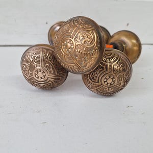 May include: Four antique brass door knobs with intricate floral designs. The knobs are round and have a raised pattern.