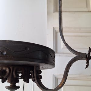 K&ouml;nnte beinhalten: Antiker Kronleuchter mit zylindrischem Schirm aus Milchglas und aufwendigen, dunklen Metallarbeiten. Das Metall weist dekorative Schn&ouml;rkel und einen gebogenen Arm auf. Die Leuchte ist f&uuml;r die Deckenbeleuchtung konzipiert.