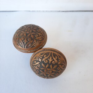 May include: Two antique door knobs with intricate floral designs. The knobs are made of a dark, aged metal with a copper tone.