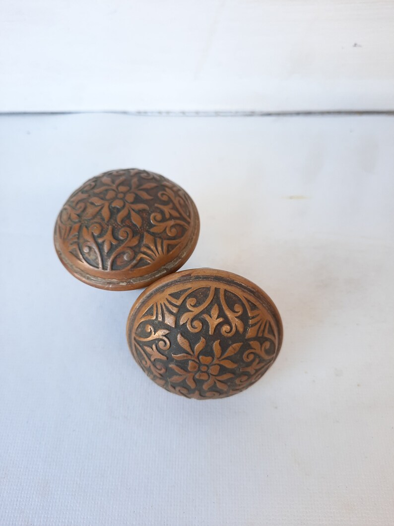 May include: Two antique door knobs with intricate floral designs. The knobs are made of a dark, aged metal with a copper tone.