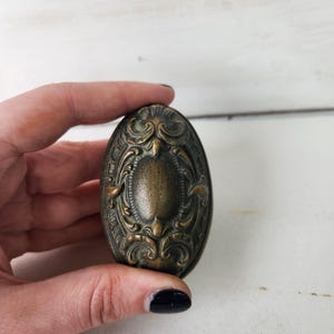 May include: An oval-shaped, ornate brass door knob with a detailed floral design.