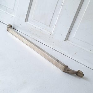 May include: A silver-toned door pull with a rectangular bar and decorative ends. The hardware is set against a white background, suggesting a vintage or antique aesthetic. The pull is approximately 24 inches long.