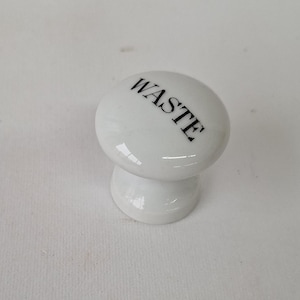 May include: White ceramic knob with a black 'WASTE' label. The knob is shaped like a mushroom with a round top and a short stem.