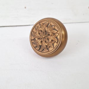 May include: A vintage brass door knob with an ornate floral design. The knob is round with a detailed pattern on the face, and a warm, antique gold finish. This decorative hardware adds a touch of elegance.
