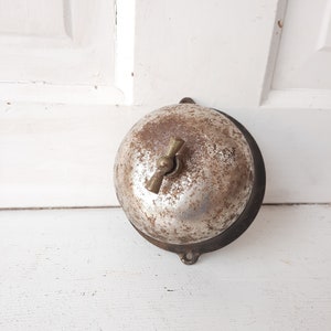 May include: A vintage silver doorbell with a brass handle. The doorbell is mounted on a white wall.